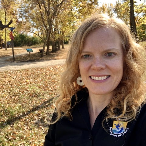 Employee wearing U.S. Fish and Wildlife Service black shirt takes selfie photo with fall foliage in the background.