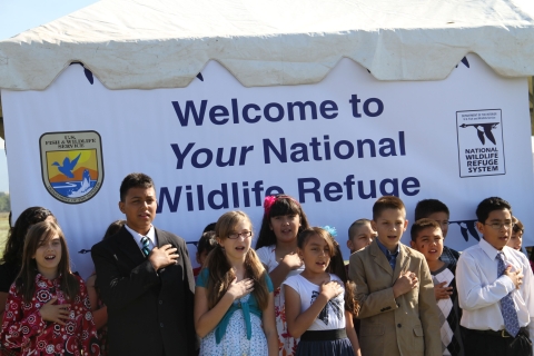 Elementary school students stand with their hands over their hearts to recite the Pledge of Allegiance at a 2012 ceremony establishing Valle de Oro National Wildlife Refuge.