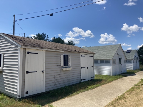 a series of three gray and white buildings next to each other with a sidewalk before them on a sunny blue sky day.