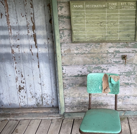 A worn green chair outside a rundown white house.