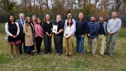 A group of people stand around a person holding a framed award certificate