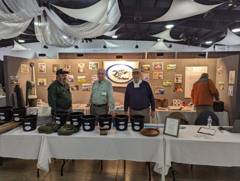 3 men behind an information booth at an event
