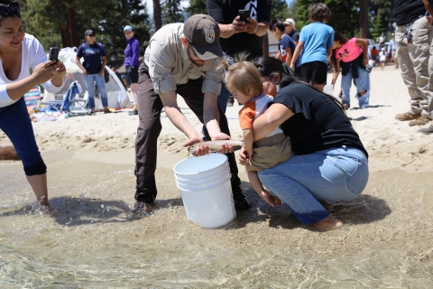 A man in a Service uniform showing a Lahontan cutthroat trout to a mother and child at a stocking event