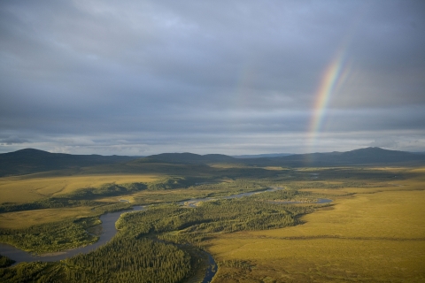 Aerial view of river valley with rainbow in the sky above.