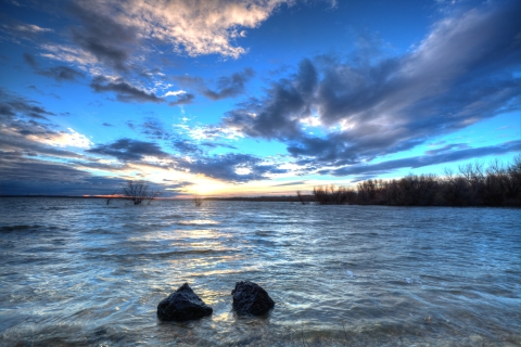 Sun just below horizon over lake with dramatic clouds above.