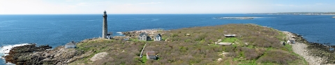 A scenic view of grassy hills and a white lighthouse on the coast of Thacher Island, with the ocean in the background
