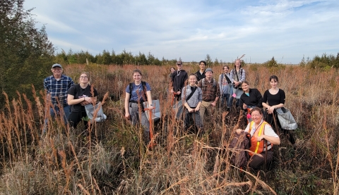 A group of people stand smiling in tallgrass outside