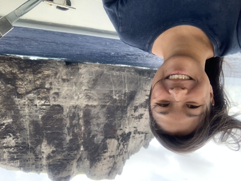 Jiny Kim, wearing a navy blue shirt, stands on a boat with Nihoa in the background.