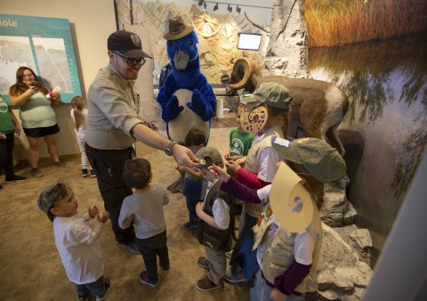 A smiling uniformed refuge ranger hands junior ranger badges out to a group of children. 