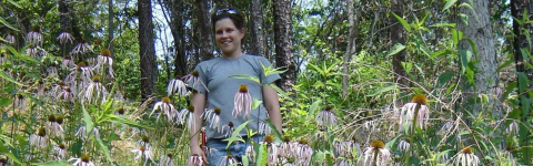 Heather Alley stands and smiles amongst tall smooth coneflower plants. The plant's petals are purple. 