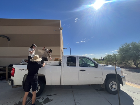 Two Service employees standing in the back of a truck preparing to unload fish from the truck's tank.