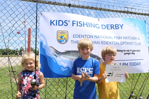 3 children in front of kids fishing derby banner at Edenton National Fish Hatchery