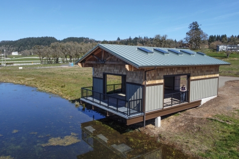 A person stands on the deck of a building next to a pond.