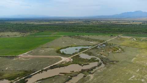 Aerial view of farmland with some wetland ponds, dirt roads, with a riparian scrub and desert mountains in the background.