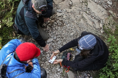 Three people seated on the ground looking at a map on a cell phone