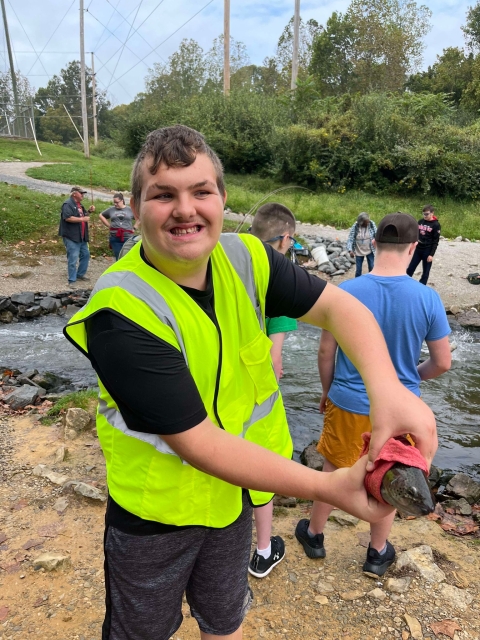 Student holding fish by stream