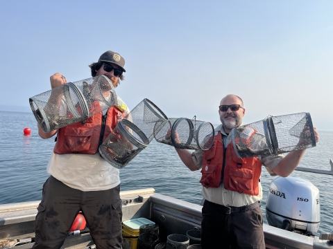 Two biologists holding up four metal minnow traps in a boat.