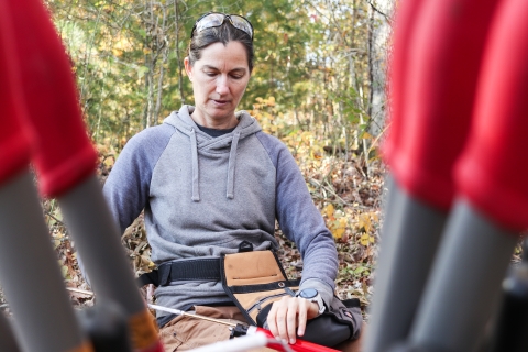 Woman holding a cylinder in one hand and pouring a tube full of small canisters into it