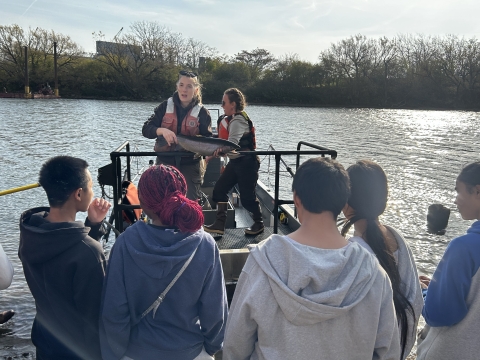 Image of biologist holding fish on boat in front of a group of students.