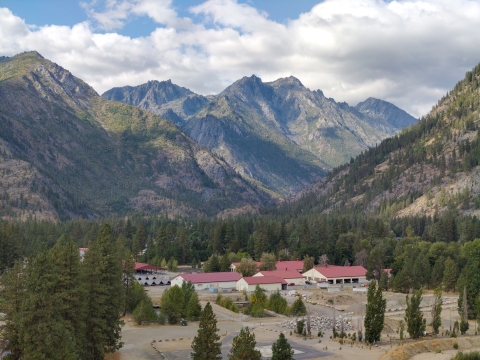 A complex of buildings with red roofs are surrounded by trees and tall mountains
