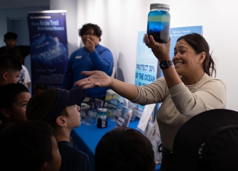 A staff shows a jar with blue color fluid to students smiling as she speaks about the Mariana Trench