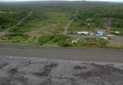 aerial view of a coast meeting a forested landscape with gravel roads and some out buildings