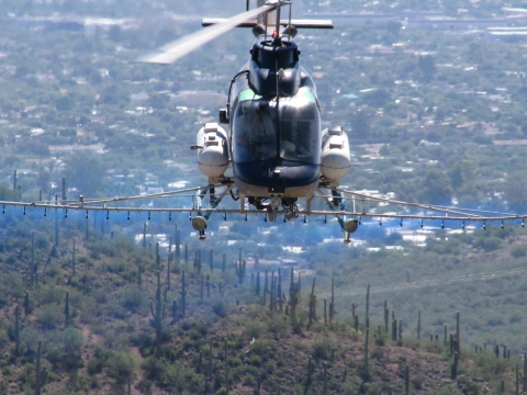 A helicopter spraying a substance over a grass and cacti covered area