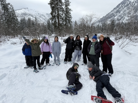 A group of 11 students gathered in snowshoes with mountains behind them
