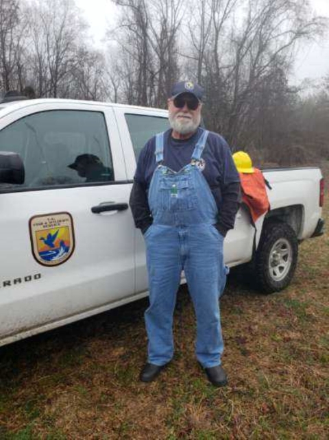 a man in overalls stands next to a white service truck
