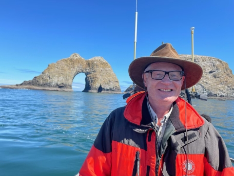 Person in boat on the ocean in front of two small rocky islands.