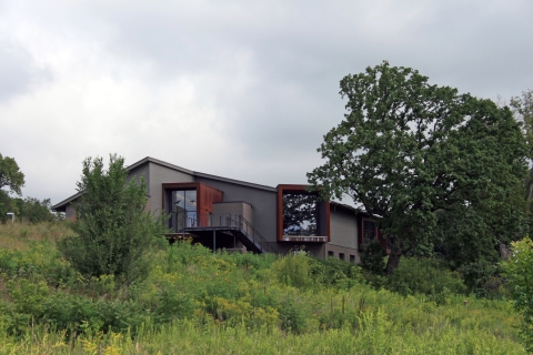A grey and brown building blends into a hillside on a cloudy day.