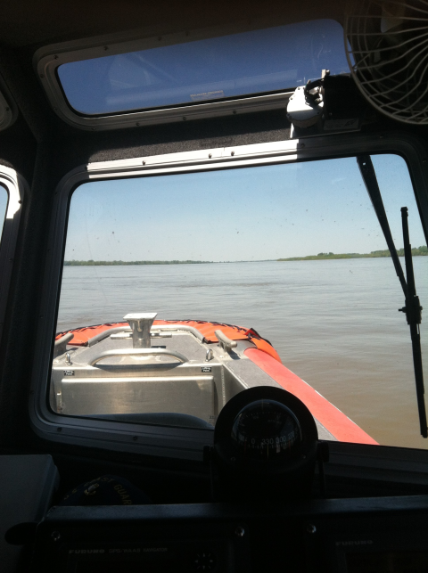 a view from the cabin of a river boat looking over the bow with a large river in the background.