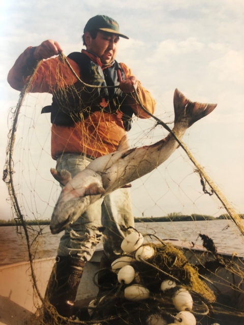 a federal wildlife biologist pulls up a gill net with a large fish in it while standing on a boat