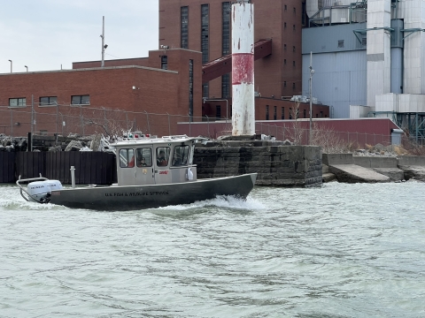 Image of work boat in waves next to an industrial shoreline.