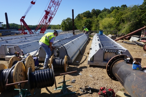 A construction crew works on assembling fish deterrent equipment on land.