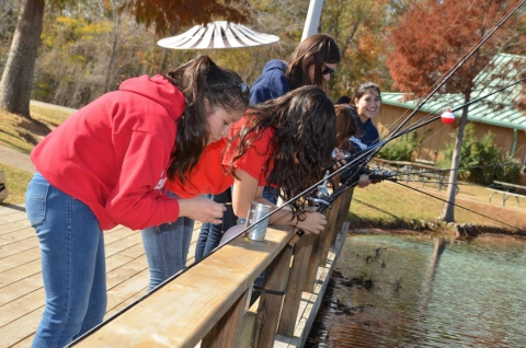 Students standing on dock fishing on the edge of a pond. 