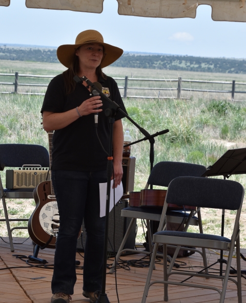 A woman in a wide-brimmed hat and Fish and Wildlife Service uniform stands on a stage with a microphone near her mouth.