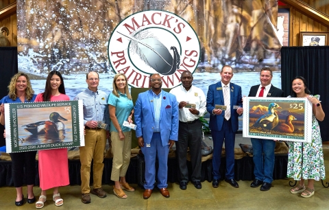9 people stand with large pictures of Duck Stamps