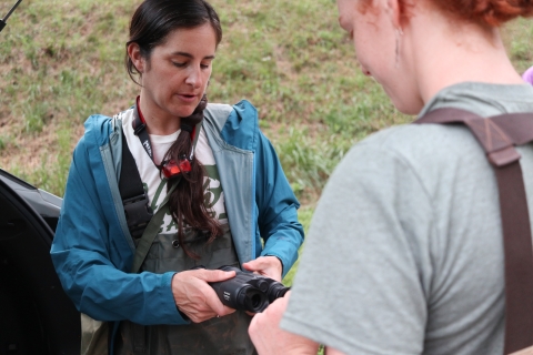 One person holding night-vision glasses speaking to a second person.