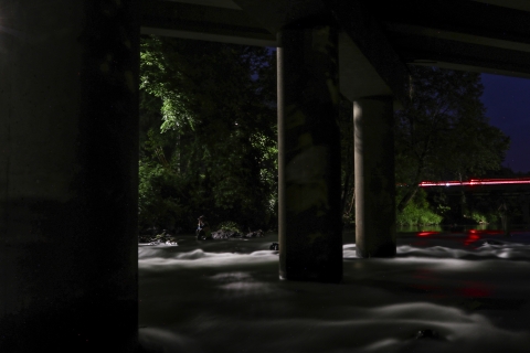 Person sitting beneath a bridge at night.