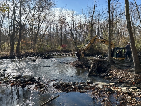 An excavator removing remnants of a dam from a river