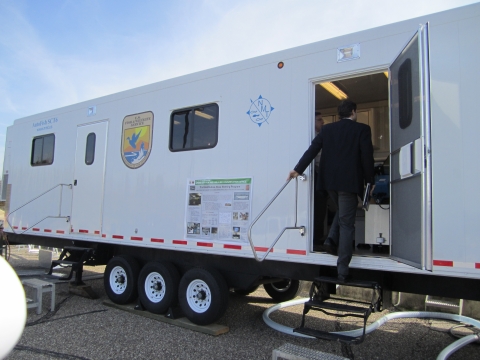 A white trailer on wheels with a U.S. Fish and Wildlife Service logo. A person climbs aboard through a side door. 