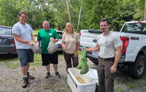 Image of 4 people holding bags of mussels next to a cooler and vehicles.