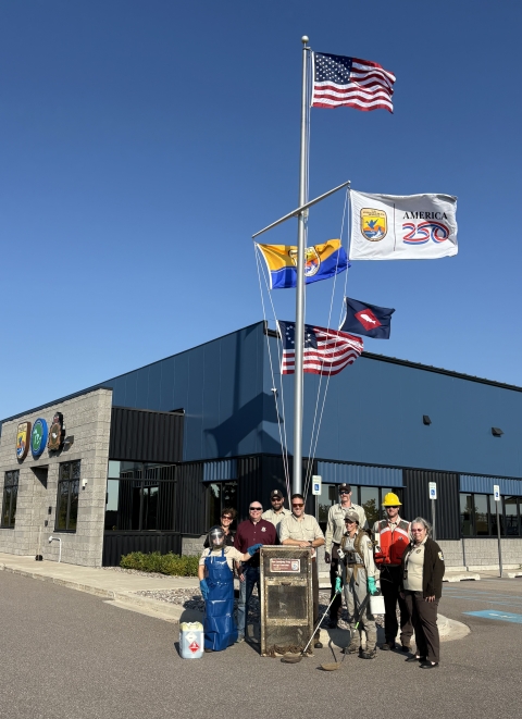 5 flags on flag pole with US at top; people stand beneath