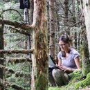 A woman crouching in a forest entering data in a computer
