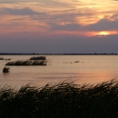 A setting sun ducks behind clouds over an expanse of open water dotted with marsh grasses