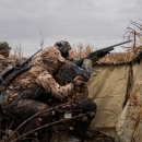 Person is camouflage hunting gear crouches behind a second person in a wheelchair in a duck hunting blind