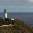 photo of a lighthouse on a bluff looking over the ocean. There is a paved path leading up to it. 