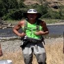 Paul Sankovich, Fish Biologist, stands in a field of tall tan grass with a stream in the background