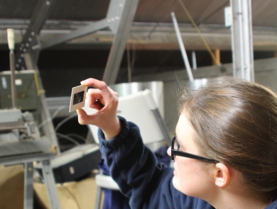 A young woman in glasses holds a slide up to look at it in an attic storage space.